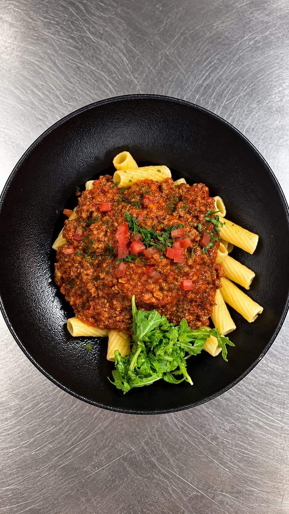 Penne bolognaise et roquette dans une assiette noire
