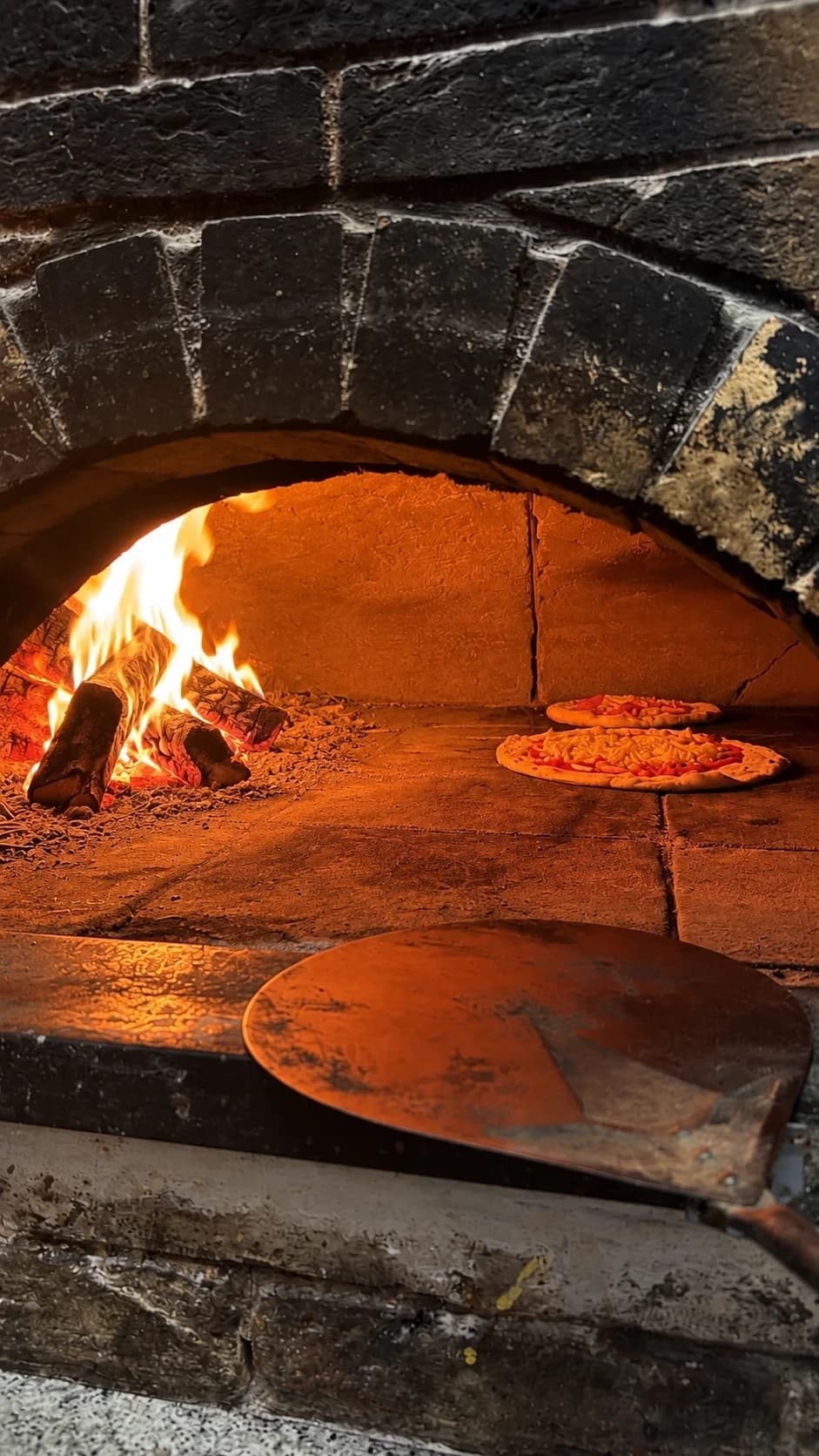 Pizzas qui cuisent dans le four à bois, à côté du feu