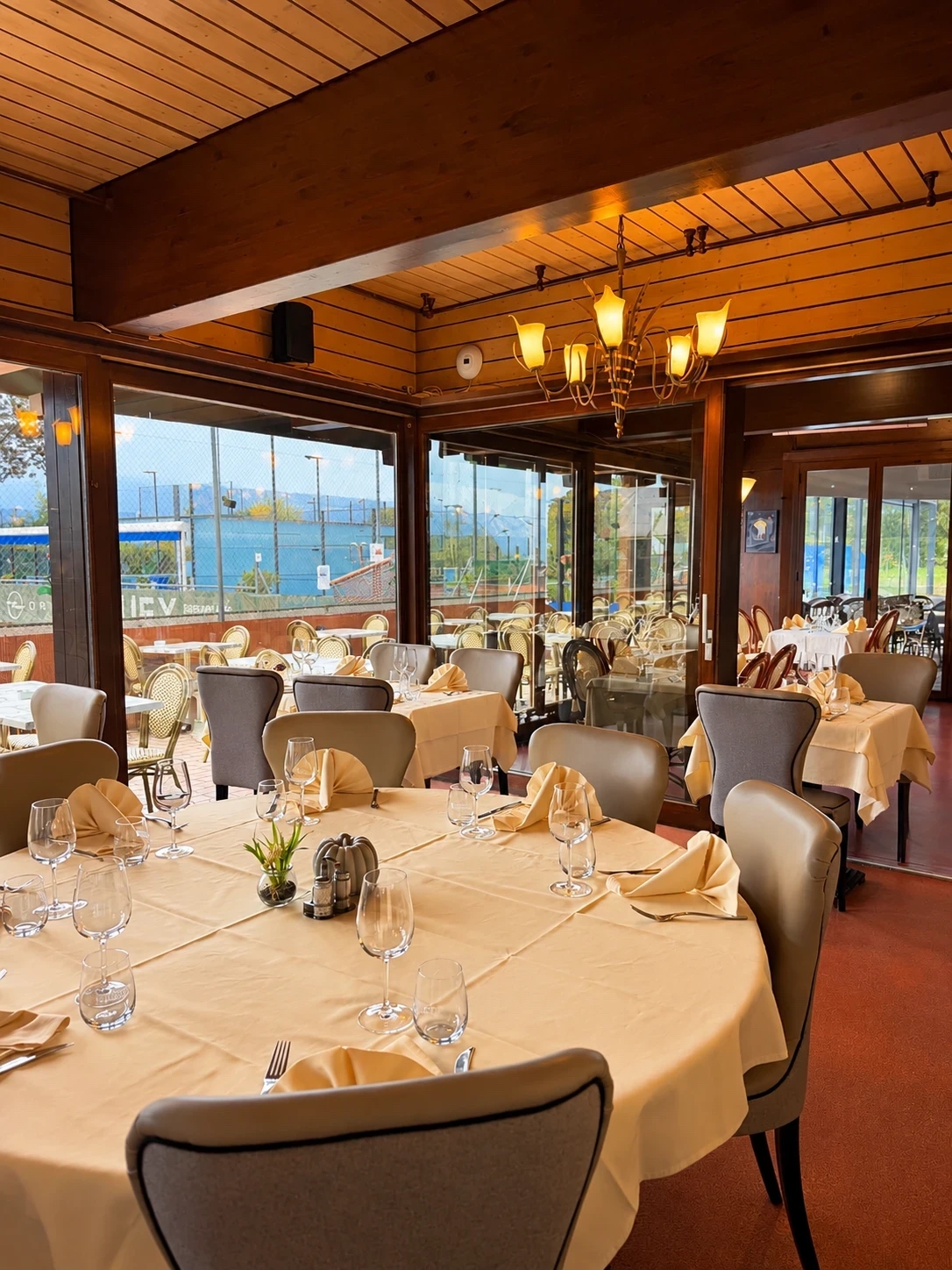 La salle du restaurant, tables dressées et grandes baies vitrées sur les courts de tennis