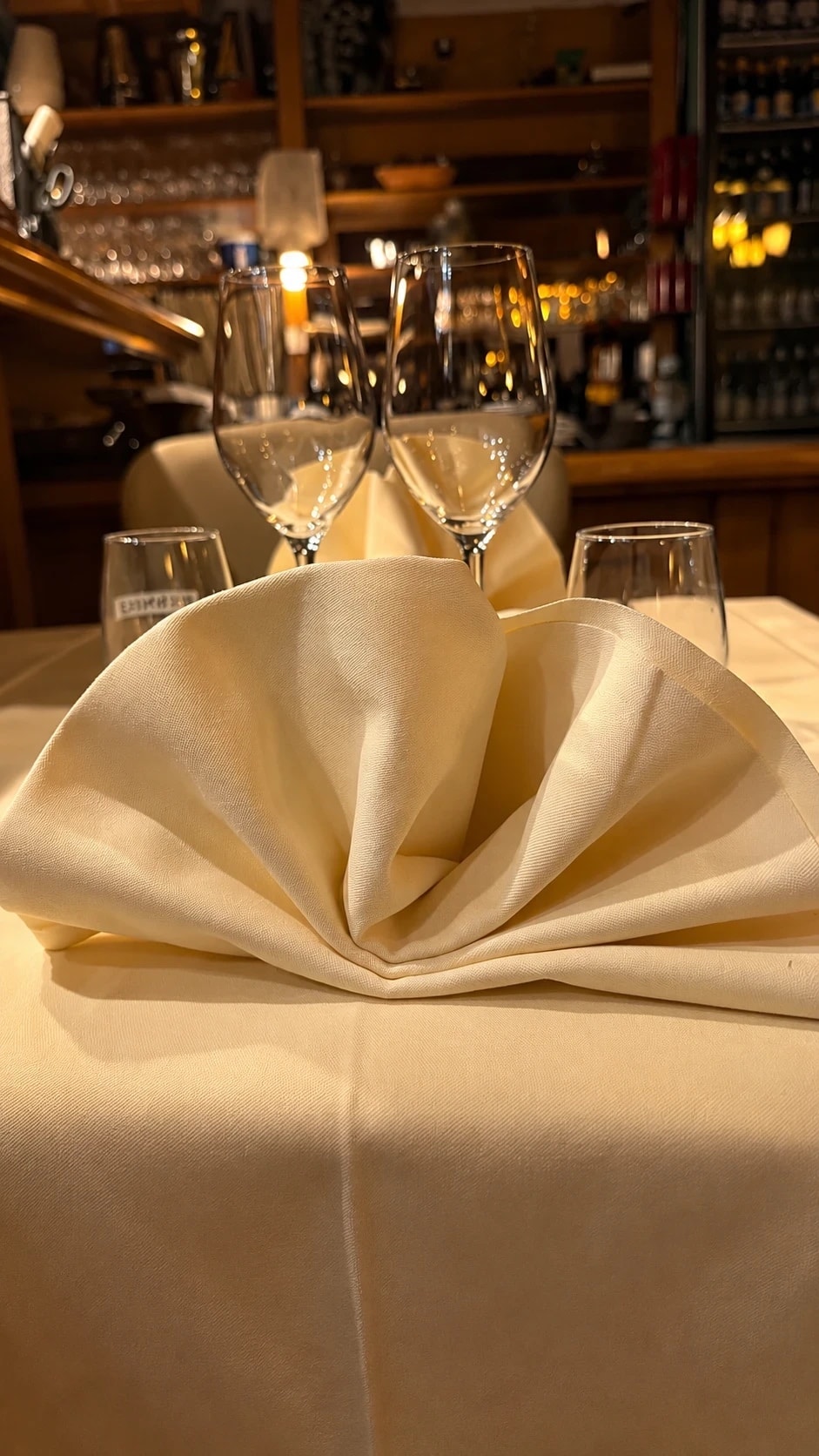 Serviette pliée et verres à vin sur une table, le bar et les bouteilles en arrière-plan